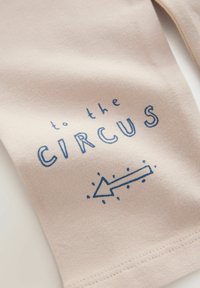 Tessuto di cotone beige con testo blu "verso il CIRCO" e una freccia rivolta a sinistra con punti, che enfatizza un design giocoso.