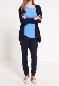 Námořnický cardigan, světle modrá blůza, námořnické jogger kalhoty a béžové podpatky. Materiál vypadá měkký s uvolněným střihem. Doplňky zahrnují dlouhé rukávy.