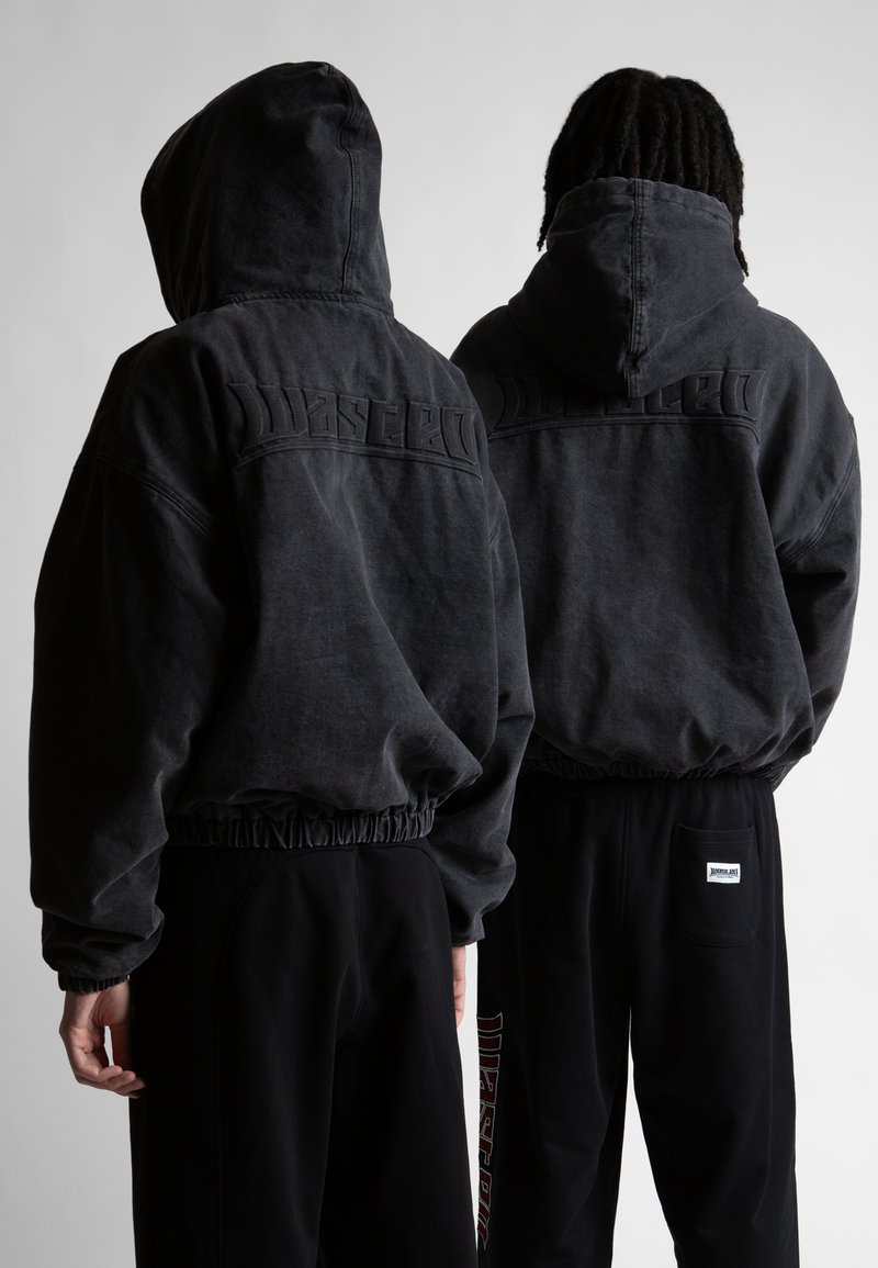 Tamsiai pilka gobtuvinė sportinė palaidinė su elastingomis rankovėmis ir apačia, rodanti iškilų "Wasted" logotipą ant nugaros. Dėvima su juodomis sportinėmis kelnėmis.