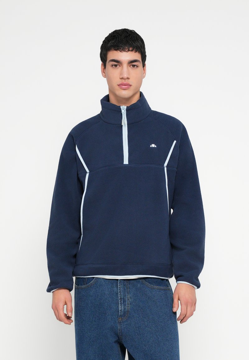 Granatowy polarowy pulower z wysokim kołnierzem, frontem na suwak do ćwiartki oraz jasnoniebieskim przeszyciem akcentującym. Z przodu na klatce piersiowej małe logo.