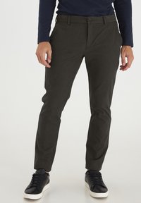Skræddersyede mørkegrønne bukser med en glat tekstur, frontknaplukning og lommer, kombineret med sorte sneakers. Lige ben design.
