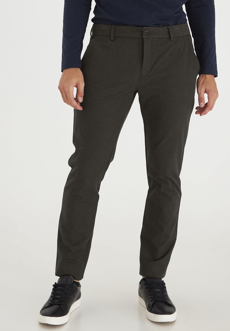 Skræddersyede mørkegrønne bukser med en glat tekstur, frontknaplukning og lommer, kombineret med sorte sneakers. Lige ben design.