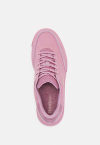 Pink athletic shoe with a textured upper, tonal stitching, lace-up design, and a cushioned insole featuring the Reebok logo.