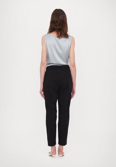 Sileeritud helesinine ilma varrukateta topp, kombineeritud mustade kitsaste pükstega, lihtne disain ja minimaalne riistvara; nähtav pahkluu beežide kontsadega.