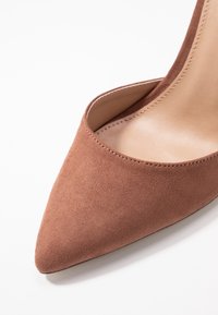 Pointed-toe high-heeled shoe in soft brown suede, featuring a low-cut vamp and a smooth beige inner lining. Accentuated stitching detail.
