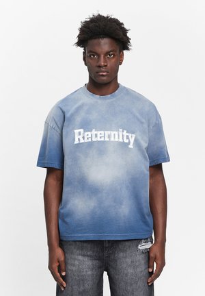 Blå gradient t-shirt med hvid "Reternity" tekst. Korte ærmer, afslappet pasform, falmet stof med blød tekstur. Båret med slidte sorte jeans.