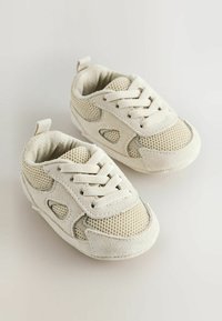 Baskets blanches pour tout-petits, fabriquées en daim et en maille. Les caractéristiques incluent des lacets, des découpes sur les côtés et une semelle texturée. Petite languette à l'arrière.