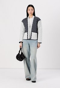 Quilted jacket in white with navy accents, featuring a geometric pattern and a cropped design. Paired with light blue wide-leg jeans and a black bag.