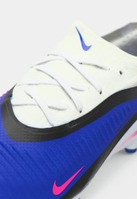 Ποδοσφαιρικό παπούτσι Nike με λευκό επάνω μέρος, μπλε και μαύρες λεπτομέρειες, υφή στη σόλα, ροζ λογότυπο και παραδοσιακό σύστημα κορδονιών.