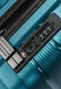 Valigia rigida blu con lucchetto a combinazione TSA a tre cifre di colore nero e due tirazip argentati.