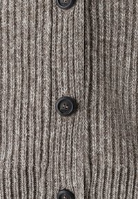Hnědý pletený kardigan má žebrovanou strukturu, černé knoflíky a směs přírodních vláken. Na knoflících je vytištěno jméno značky "MAERZ."