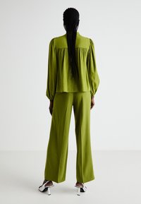 Grön texturerad topp med puffärmar, parat med vida gröna byxor. Noterbara blanka vita klackar med blockklackdesign.