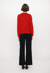 Red knitted sweater with a ribbed hem and long sleeves, paired with black wide-leg trousers. Smooth texture, no visible patterns or accents.