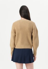 Strikkegenser i beige med løs passform, ribbestrikkede mansjetter og rund hals, sammen med et plissert marineblå skjørt.