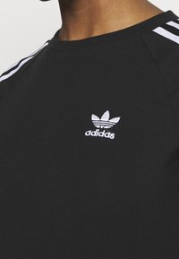 Czarna bawełniana koszulka z okrągłym wycięciem, krótkimi rękawami oraz białym logo Adidas z motywem trefoil na lewej piersi.