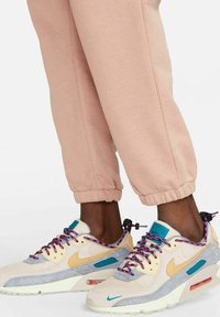 Nike Air Max-sneakers med beige meshtopp, ljusgrå mockadetaljer, lila och turkosa snören, och synlig luftkudde i sulan.