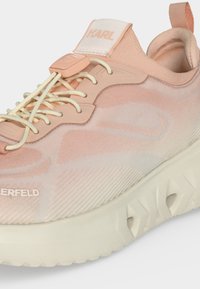 Baskets rose clair avec semelle blanche, système de laçage élastique, languette de tirage au talon et marquage sur la languette et le côté.