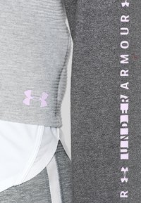 Vêtements de sport en tissu gris avec texture côtelée et un panneau blanc. Détail de logo et de texte en rose sur le côté. Matériau doux et extensible.