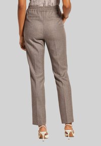 Op maat gemaakte bruine broek met een subtiele visgraatpatroon, elastische tailleband en slim fit, gecombineerd met beige hoge hakken met bandjes.
