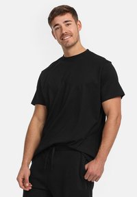 T-shirt noir à manches courtes avec un col rond, fabriqué en coton. Design simple sans motifs ni accents. Coupe ajustée aux épaules.