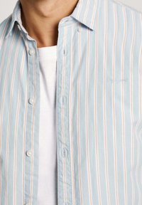 Jasnoniebieska koszula w paski z białymi i subtelnie pomarańczowymi liniami, zapinana na guziki, wykonana z miękkiego materiału, z małym haftowanym logo.