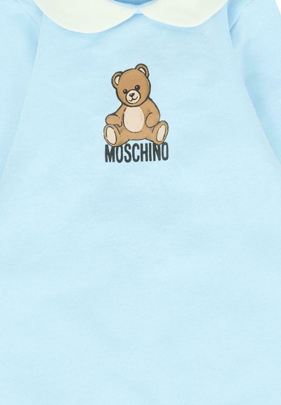 Hellblaues Babykleidungsstück mit einem Teddybär-Design über dem Wort "MOSCHINO" in schwarzen Buchstaben auf der Vorderseite.