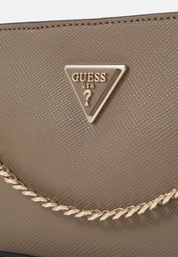 Guess USA-handveske i teksturert taupe-materiale med gull trekantlogo. Har en gullkjedeakzent langs kanten.