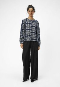 Blusa navy con estampado floral, escote redondo y hombros fruncidos; combinada con pantalones de pierna ancha negros de cintura alta y tacones de punta.