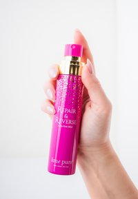 Lyserød sprayflaske med guld detaljer, mærket "Repair & Reverse Ultra-fine Mist." Har en fin tåge dyse og en glat tekstur.