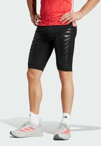 Zwarte sportshorts met een gestructureerd, gestreept patroon. Slanke pasvorm, gecombineerd met grijze en roze hardloopschoenen en witte sokken.