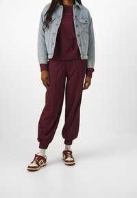Sudadera burdeos y joggers a juego con un corte relajado, combinados con una chaqueta de mezclilla azul claro y zapatillas burdeos.