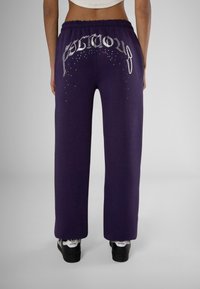 Paarse trainingsbroek met een elastische tailleband, voorzien van een zilveren logo en strasstenen versieringen op de achterkant, relaxte pasvorm.