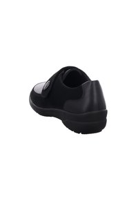 Black shoe made of leather and suede, featuring a Velcro strap, rounded shape, and textured sole. Minimalistic design with a smooth finish.