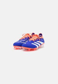 Blauwe voetbalschoenen met oranje veters, witte strepen en doorzichtige noppen. Getextureerd bovenmateriaal voor grip en flexibiliteit.
