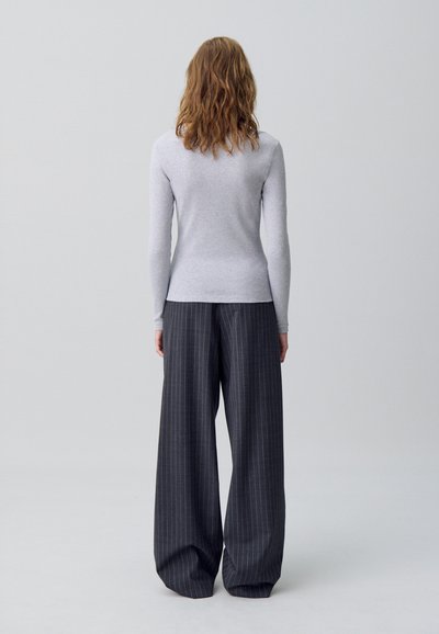 Maglia grigia a maniche lunghe con una vestibilità slim abbinata a pantaloni scuri a gamba larga a vita alta, caratterizzati da un sottile motivo a righe.