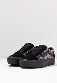 Schwarze Wildleder-Sneaker mit rosa und violetten, flauschigen Akzenten, runden Schnürsenkeln, flacher Gummisohle und einem kontrastierenden Seitenstreifendesign.