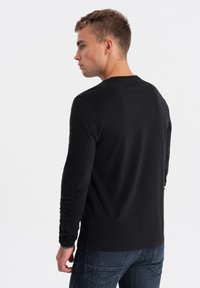 Langärmliges schwarzes T-Shirt aus weichem Stoff, mit Rundhalsausschnitt und minimalistischem Design, kombiniert mit dunkelblauen strukturierten Jeans.