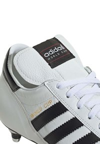 White leather soccer cleat with black stripes, lace-up design, padded tongue, gold "WORLD CUP" lettering, and molded studded outsole.
