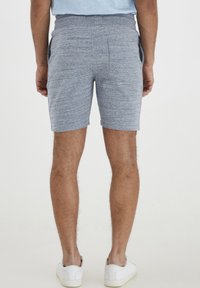 Pantalones cortos grises y texturizados con un corte relajado y bolsillos laterales, que cuentan con una cintura elástica ajustable. Combinados con zapatillas blancas.