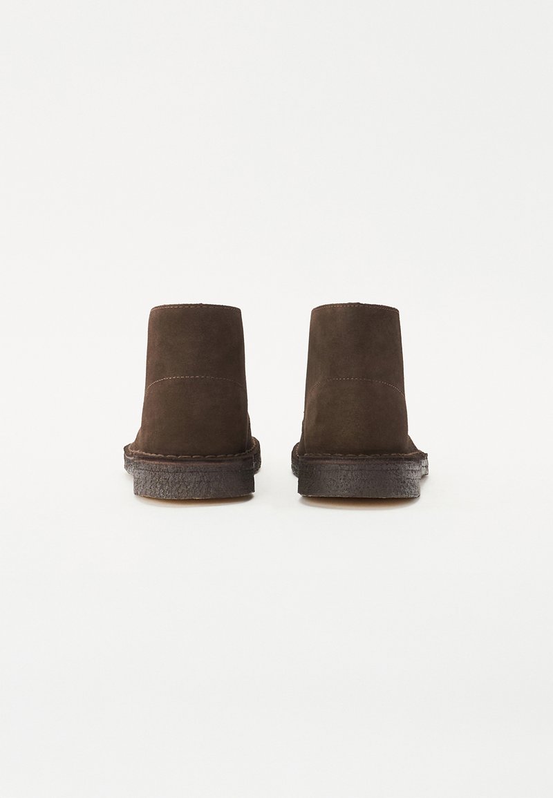 Bruine suede enkellaarzen met een platte zool, met een clean ontwerp en minimale stiksels langs de randen. Geen zichtbare hardware of accenten.