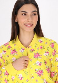 Giacca bomber gialla con stampa floreale in rosa e bianco. Chiusura con zip e colletto e polsini a coste. Tessuto liscio e leggero.