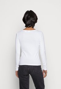 Langarm, nauwsluitend wit katoenen top met een ronde hals en een gladde textuur. Gecombineerd met donkergrijze broek, met minimale ontwerpelementen.