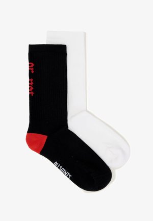 Een paar sokken, één zwarte met een rode hiel en witte tekst, één effen witte, plat gelegd en overlappend.