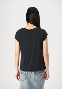 Svart kortermet topp med rund hals, laget av glatt stoff. Brukt sammen med en lys blå denimskjørt med baklommer.