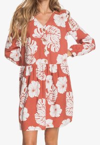Czerwona sukienka w kwiaty z białymi wzorami hibiskusa i liści, z długimi rękawami, dekoltem w kształcie litery V, zapięciem na guziki z przodu oraz marszczoną talią dla swobodnego dopasowania.