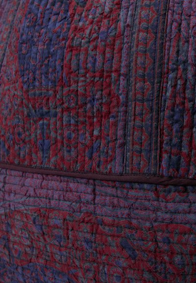 Prešívaná látka s hlbokými červenými a námorníckymi modrými odtieňmi, s zložitými textilnými vzormi a textúrami, ktoré vytvárajú vrstvený, dimenzionálny vzhľad.