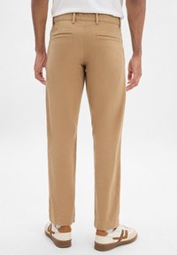 Chinos beige con gamba dritta e due tasche posteriori, abbinati a sneakers bianche e beige. Il tessuto ha una consistenza liscia.