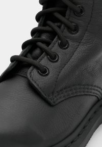Bota de cuero negra con punta redondeada, ojales de metal, cordones planos y detalle de costura en la parte superior y los laterales. Textura suave.