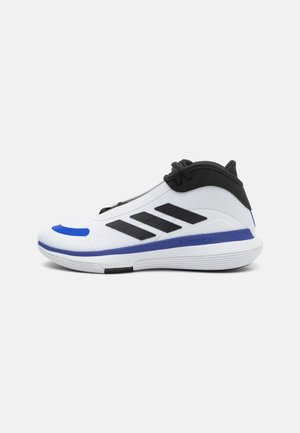 Zapato deportivo blanco con detalles en negro y tres franjas diagonales. Presenta una textura suave, punta redondeada y suela exterior morada.