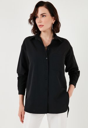 Black button-up shirt with a collar, long sleeves, chest pocket, and a relaxed fit. Made of smooth fabric with subtle sheen.